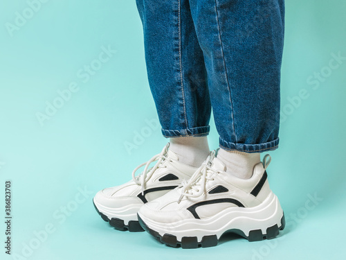 Legs of a stylishly dressed child in wide jeans and white sneakers. Place for text. © kvladimirv