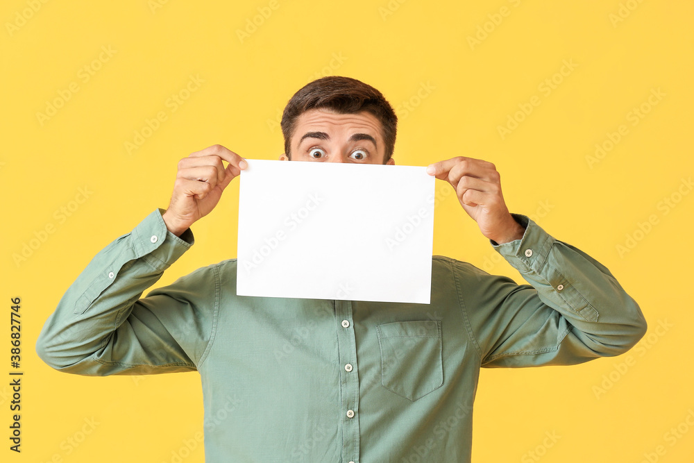 Surprised young man with blank paper sheet on color background Surprised young man with blank paper sheet on color background