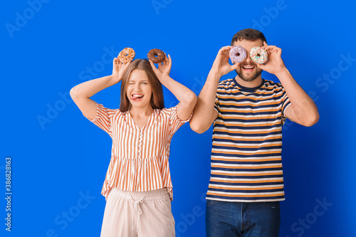 Young couple with sweet donuts on color background © Pixel-Shot