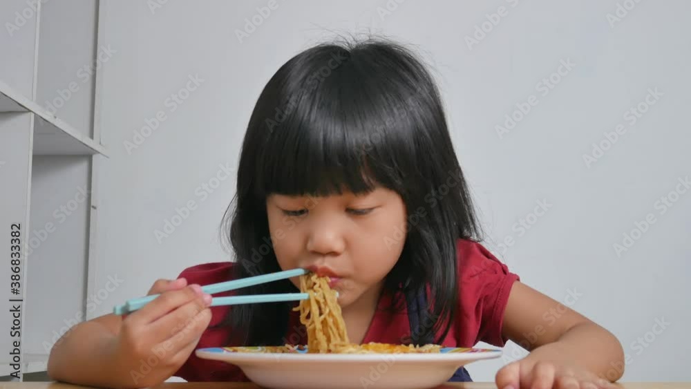 Asian baby girl enjoys noodles, little kid using chopstick to eat her meal Asian baby girl enjoys noodles, little kid using chopstick to eat her meal