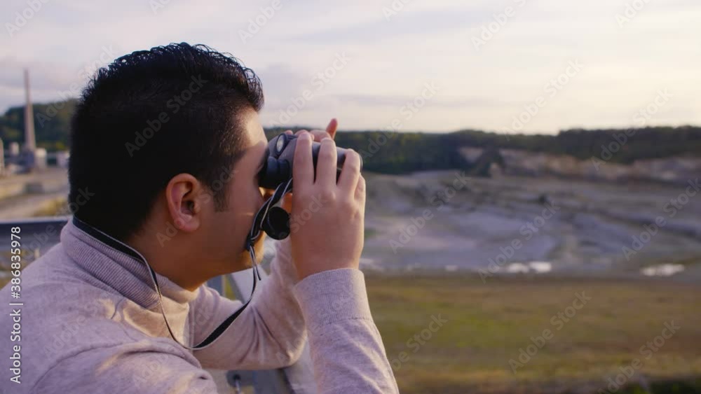 A young man looking over a beautiful scenery of a quarry with binoculars A young man looking over a beautiful scenery of a quarry with binoculars