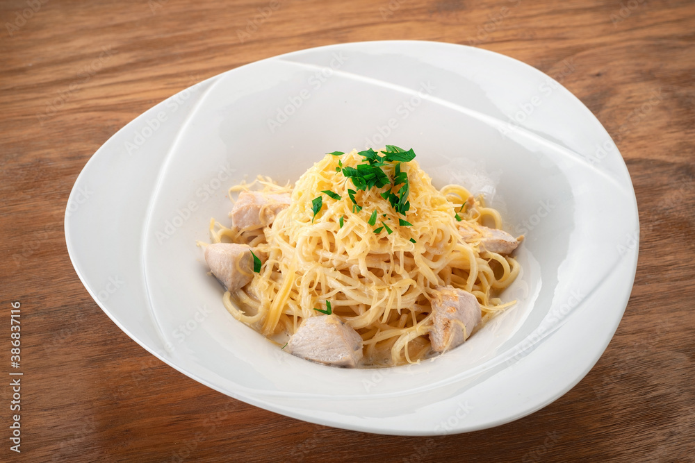 Alfredo spaghetti pasta with chicken fillet and sauce on a white plate on a wooden background Alfredo spaghetti pasta with chicken fillet and sauce on a white plate on a wooden background