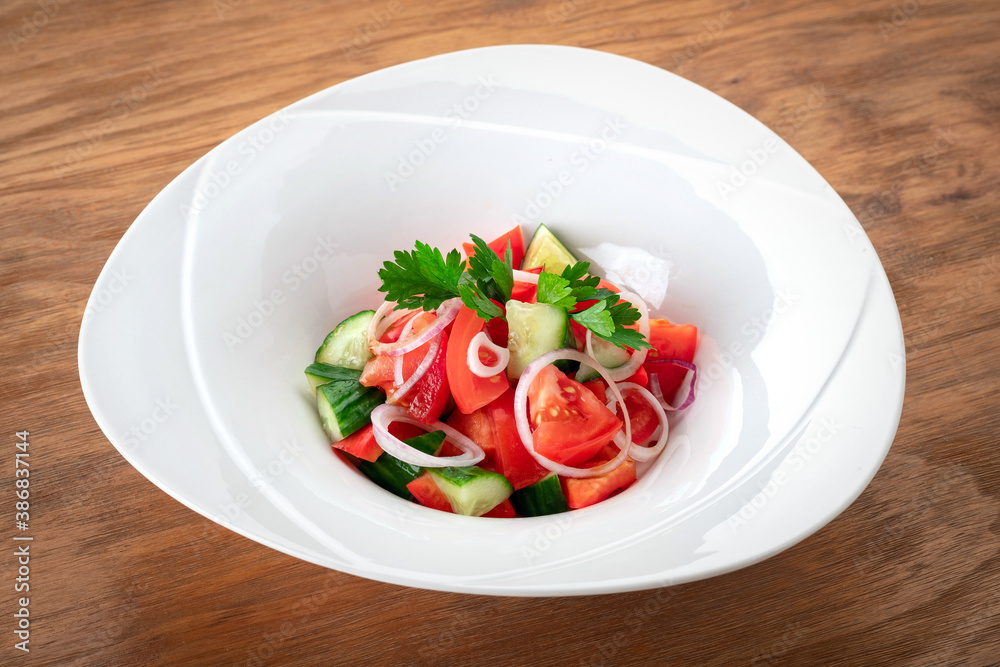 Fresh summer vegetable salad with tomatoes, cucumbers, onions and parsley in a white bowl on a wooden background Fresh summer vegetable salad with tomatoes, cucumbers, onions and parsley in a white bowl on a wooden background
