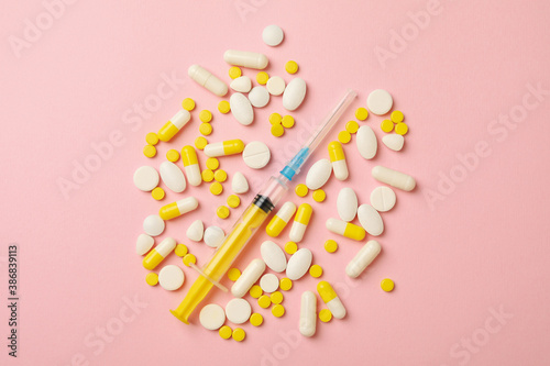 Pills and syringe on pink background, top view