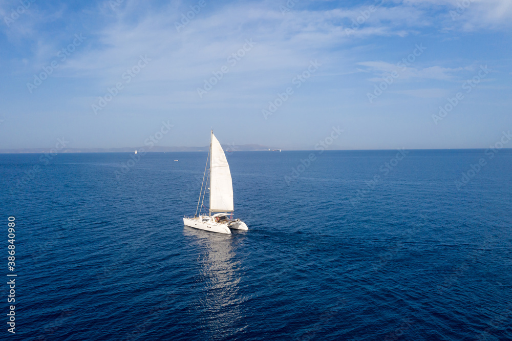 Sailing boat catamaran with white sails, cloudy sky and rippled sea background