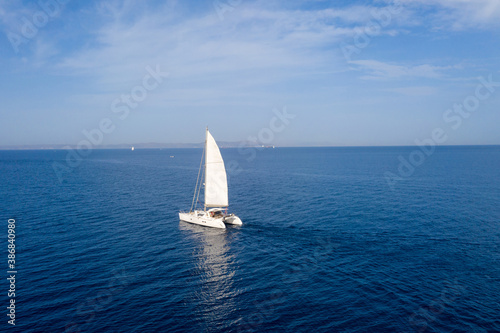 Sailing boat catamaran with white sails, cloudy sky and rippled sea background
