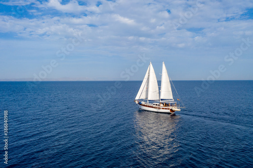 Sailing boat with white sails in the open sea, cloudy blue sky