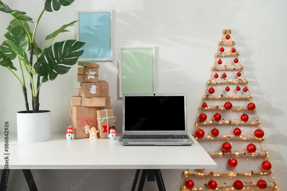 Christmas online shopping concept. Laptop and gifts on a white desk, original Christmas tree from branches in a home office. Morning sunshine. - obrazy, fototapety, plakaty 