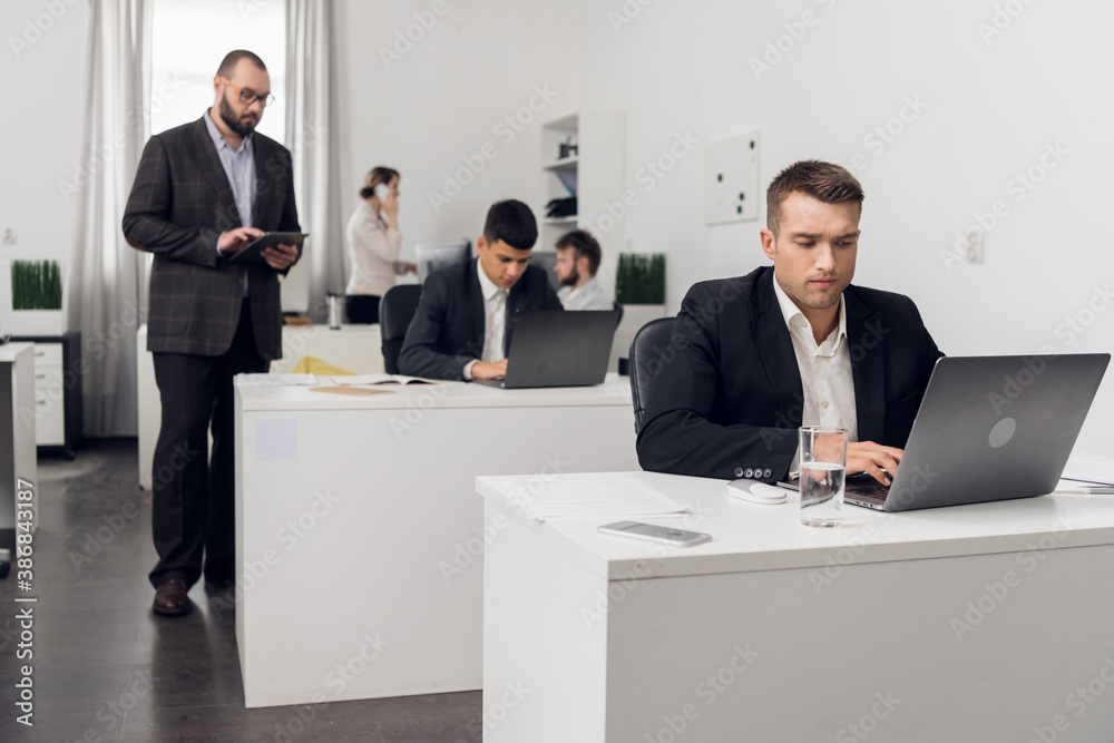 The senior Manager checks the quality of tasks performed by his Junior employees sitting at a computer in the office of a financial company. The senior Manager checks the quality of tasks performed by his Junior employees sitting at a computer in the office of a financial company.