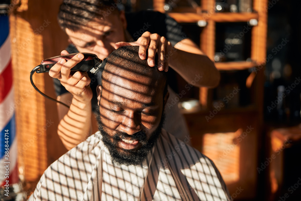 Smiling Afro American young man getting haircut in barbershop