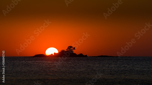 sunset on the sea behind a small island. The peaceful landscape of sunset at the horizon line makes the beautiful orange and black scene of golden hour.