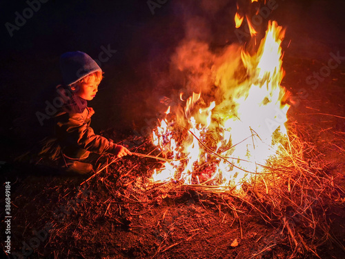 Happy caucasian boy straightens burning coals in campfire