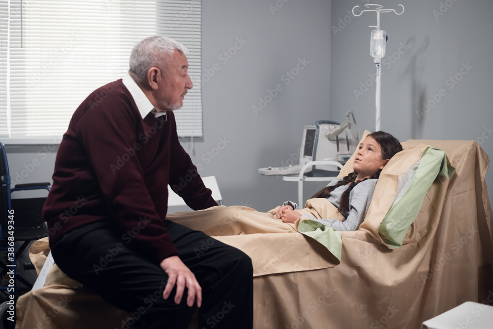 Obraz premium A senior man sitting beside a child in a hospital ward.