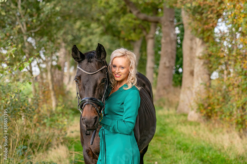 Happy beautiful blond girl in a green dress, cuddling her horse outdoors. Selective focus on the horse, autumn colos. Narrow depth of field, copy-space