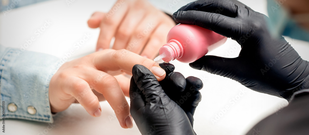 Nail treatment by cuticle oil while manicure of young woman in nail salon