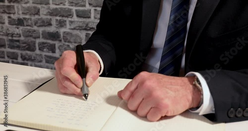 Close up to business man with glasses focusd on writing in notebook on office desk photo