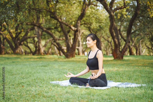 Young attractive woman meditating in lotus position sitting on the grass in the park. Yoga and harmony concept © Artem