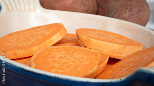 Sliced sweet potato on top of each other in a ceramic casserole. The bright orange herb staple is a healthy replacement for potato or french fries. Concept for displaying food in fall colors.