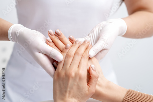Manicurist wearing gloves doing wax massage on female hands with manicure in nail salon