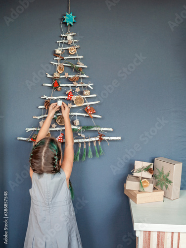 Girl near original Christmas tree made with branches, ecological toys, zero waste holidays photo