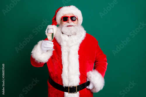 Portrait of his he nice attractive handsome cheerful cheery Santa father drinking champagne having fun saying congrats toast festive day isolated over green color background