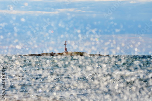 View of a small island lighthouse in the Mediterranean behind the water splinters