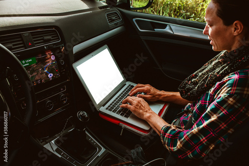 Woman using a laptop inside a car, on the co-pilot seat. White screen.