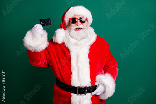 Photo of pensioner stylish grandfather grey hair hand belt hold credit card offer honest mortgage wear red santa x-mas costume coat gloves sunglass cap isolated green color background