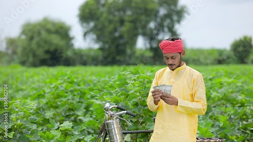 Happy Young Indian farmer counting money at cotton field