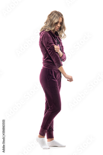 Young woman at home in socks getting dressed in burgundy tracksuit leisurewear. Full body isolated on white background.