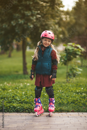 Portrait of a cute girl on rollers and wearing a helmet. Leisure riding in the park.