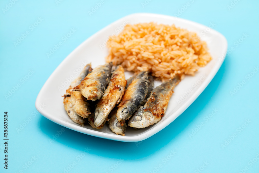 fried small sardines with tomato rice on white dish on blue background fried small sardines with tomato rice on white dish on blue background