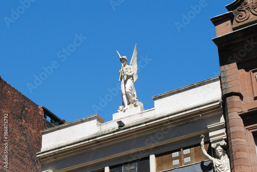 Isolated White Carved Stone Winged Figure on Facade of Old Building against Blue Sky 