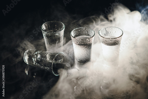 Obraz na płótnie Close-up view of bottle of vodka with glasses standing on ice on black