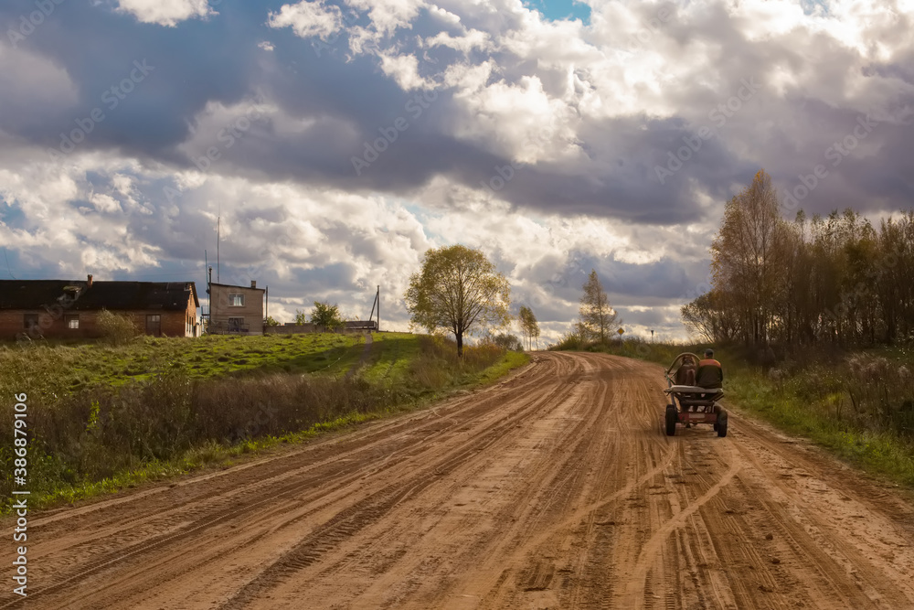 An empty country road in Belarus in a cloudy sunny day with a man in horse cart.