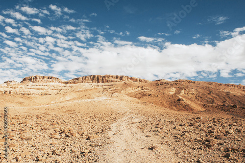 Ramon crater landscape. Travel through the Israel desert. Sunny day on dry sandy desert. Great heat on hiking path. High mountain to climb.