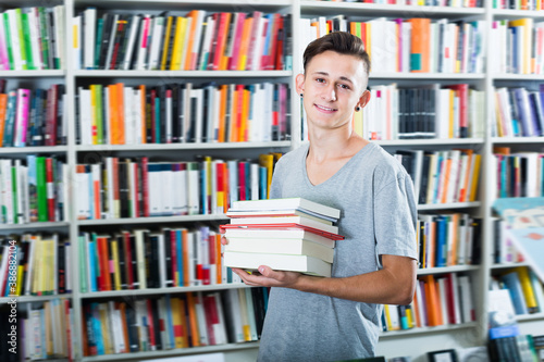 Portrait of cheerful teenager boy with book pile in shop