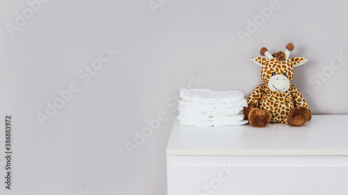 Children's stuffed toy giraffe and baby diapers on a gray background copi space