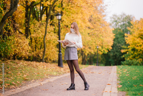 Young woman protecting from corona virus when walking in park. Autumn background.