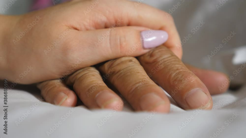 Granddaughter takes and gently touches wrinkled arm of sick mature grandma lying in bed hospital. Girl comforts hand of her old grandmother in medical clinic. Daughter gives support to her mother Granddaughter takes and gently touches wrinkled arm of sick mature grandma lying in bed hospital. Girl comforts hand of her old grandmother in medical clinic. Daughter gives support to her mother