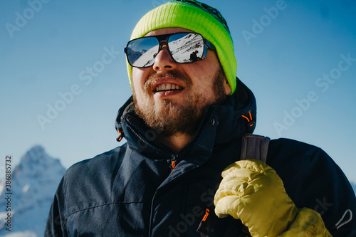 Photo of a happy man in winter clothes and ski goggles on the top of the mountain. Photo tourist snowboarder.