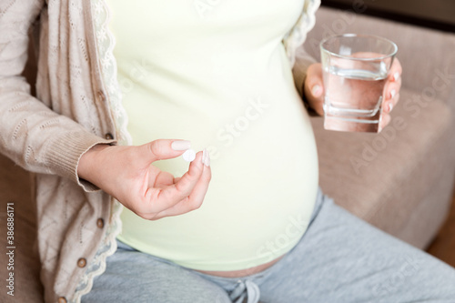 pregnant woman is sitting in sofa. Taking pills from colds. Last months of pregnancy