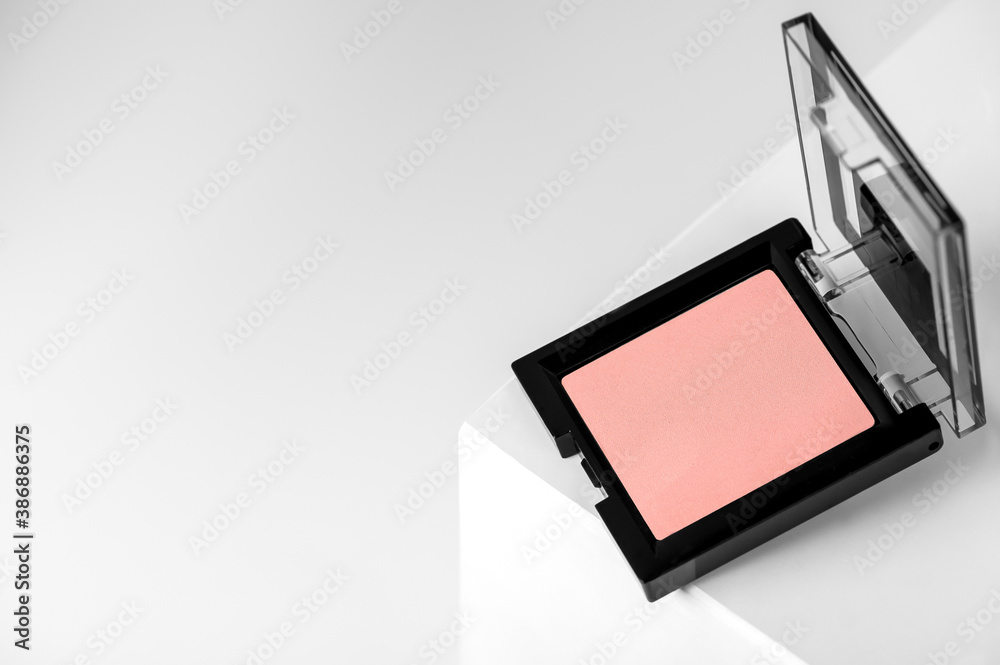 Compact pink blush on a geometric gray background close-up. Makeup beauty is a mineral product with a powdery texture. Concealer in an open black container on the podium.