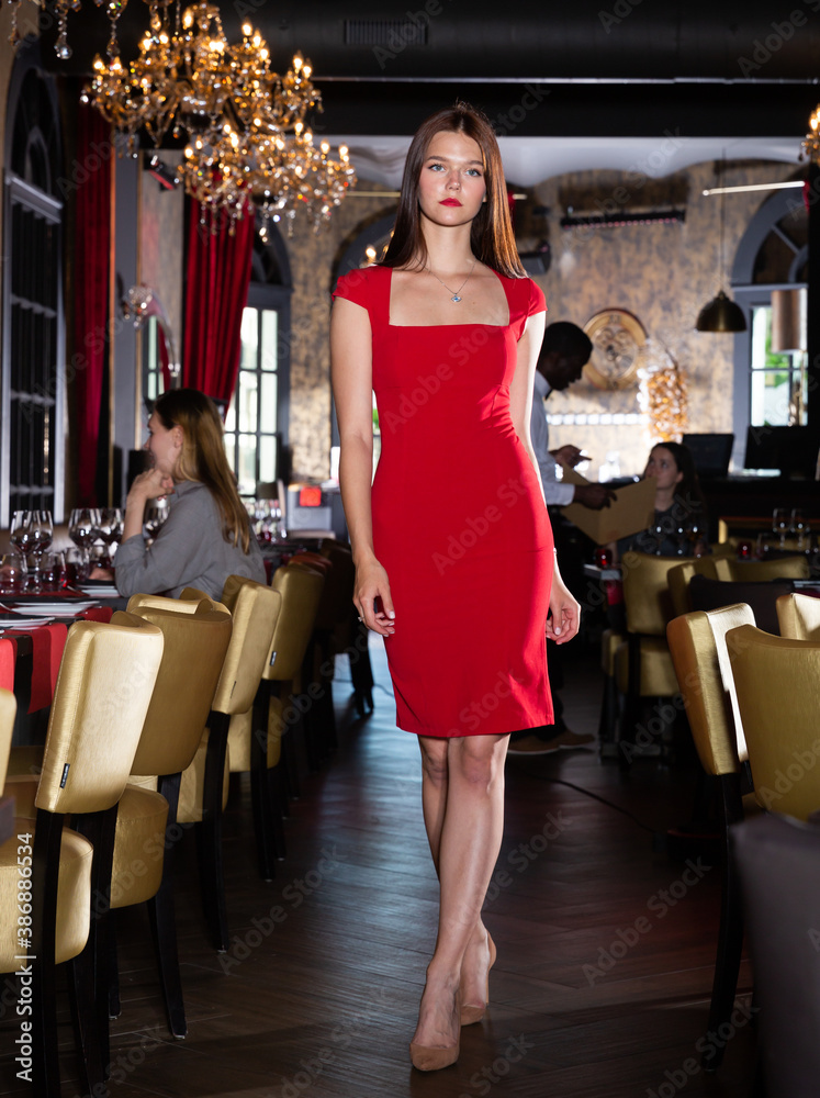 Portrait of beautiful young woman in elegant red dress walking in restaurant.Smiling pretty girl in red Evening Dress walking in luxury restaurant