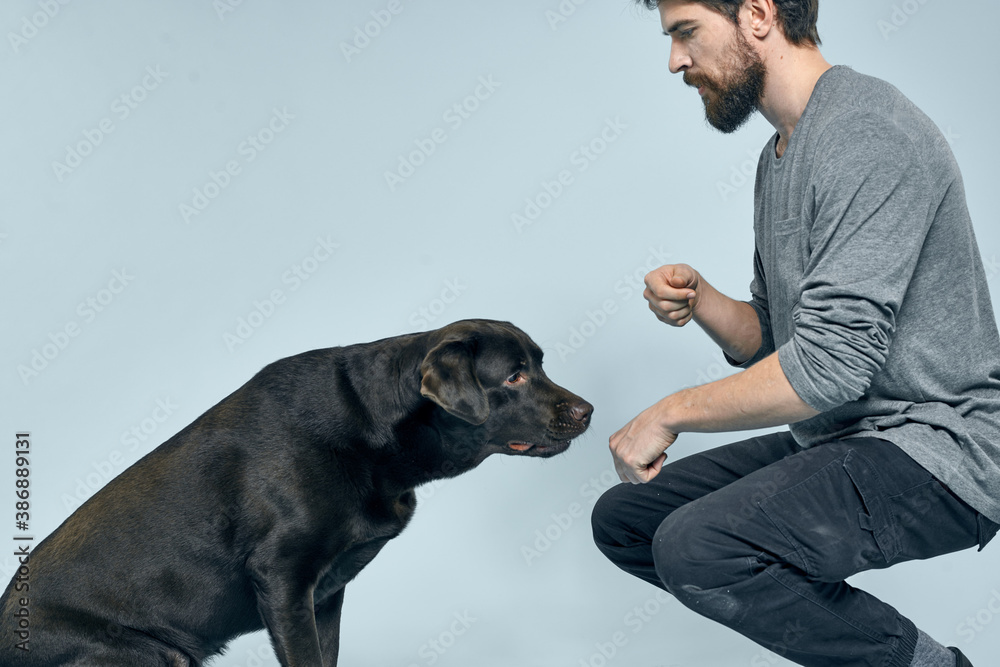 The man trains the dog indoors and gestures with his hands to execute the model's commands The man trains the dog indoors and gestures with his hands to execute the model's commands