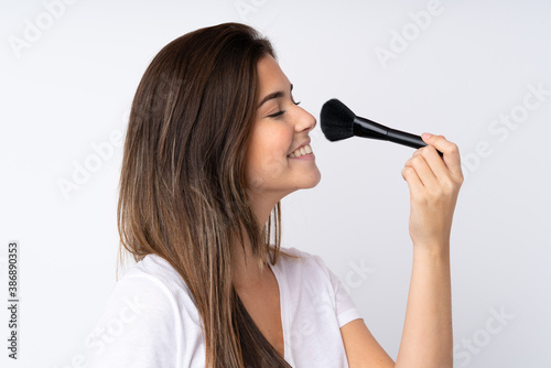 Teenager girl over isolated background holding makeup brush and whit happy expression