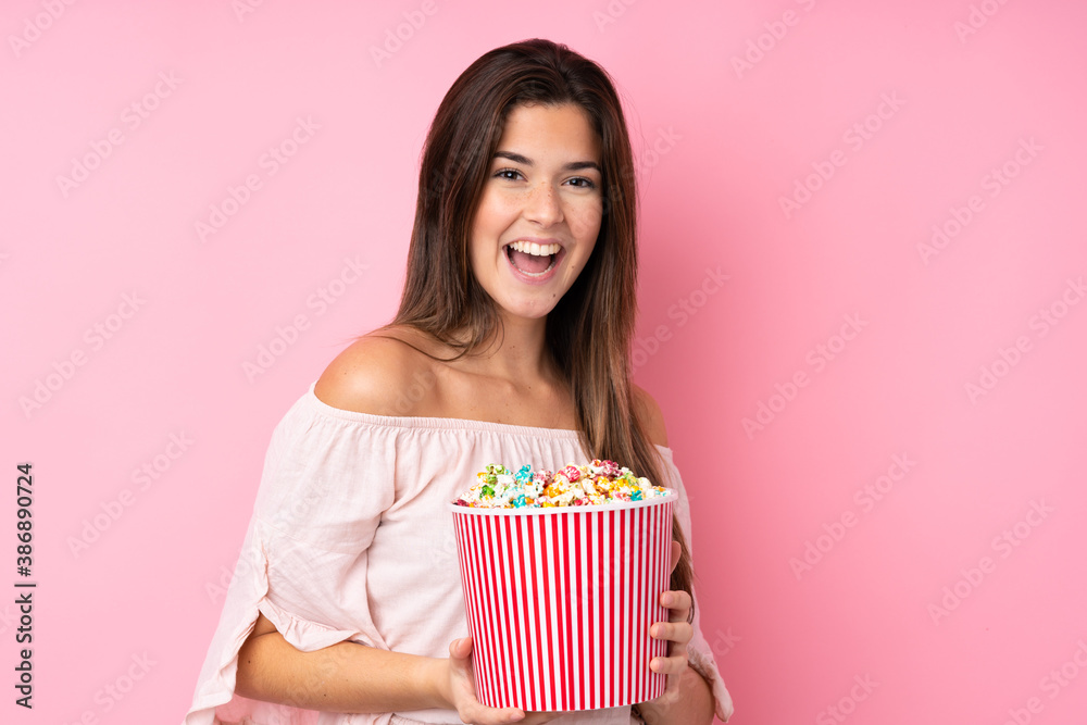Teenager girl over isolated pink background holding a big bucket of popcorns Teenager girl over isolated pink background holding a big bucket of popcorns