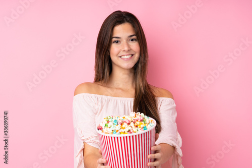 Teenager girl over isolated pink background holding a big bucket of popcorns