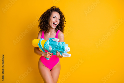 Photo portrait of woman holding water gun ready to fight laughing wearing pink swim wear isolated on bright yellow colored background © deagreez