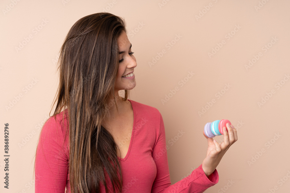 Teenager girl over isolated background holding colorful French macarons and happy Teenager girl over isolated background holding colorful French macarons and happy